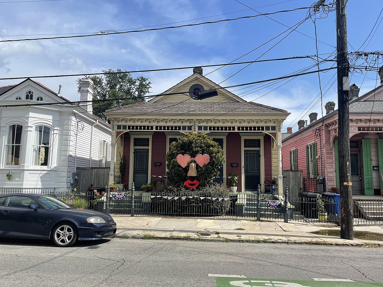The 2300 block of Royal Street. Three cottages side by side in white, red and pink, low iron fences along the sidewalk, and a shrub in one front garden clipped and dressed to look like a face.