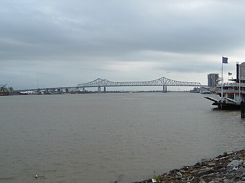 The Mississippi from the levee at the foot of St. Peter Street on a grey day, a steel bridge across the water behind and a sternwheeler moored at the right.