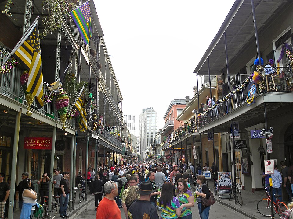Royal Street full of people in Carnival season. Flags and beads hung along the galleries, art dealers and shops at street level.