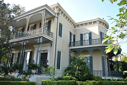 The house at 1448 Fourth Street, cream stucco with deep cast iron galleries on two floors and two sides and a rounded bay at the corner.