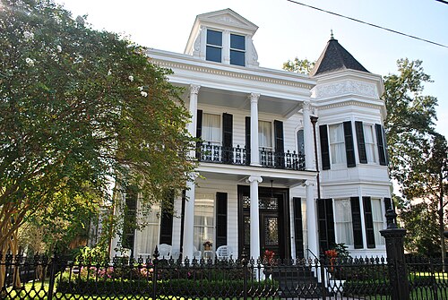 A white house on Prytania Street with Corinthian columns on both floors, an octagonal tower at one end and a cast iron fence along the sidewalk.