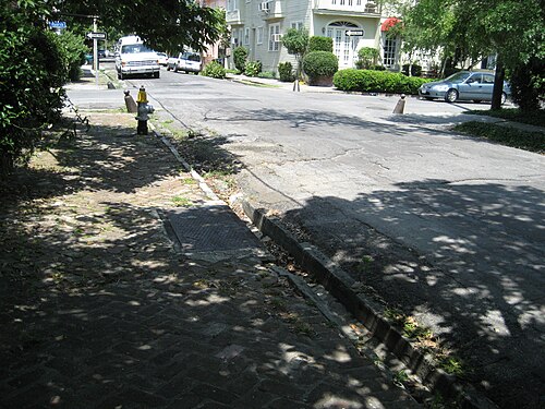 A corner on Fourth Street with a brick sidewalk, a stone gutter, an iron grating over the drain and cast iron posts at the kerb.