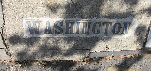 The name WASHINGTON spelled in blue and white tiles set into a cracked concrete sidewalk.
