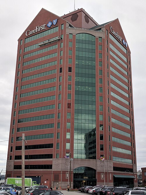 A tall red brick and green glass office tower on the Canton waterfront, CareFirst signage across the top and a surface parking lot at its base.