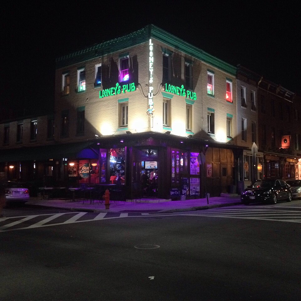 Looney's Pub lit up at night, green neon signage wrapping a three storey brick corner building facing the square.