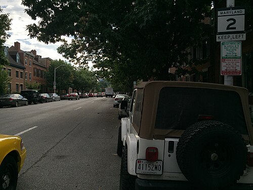 Montgomery Street looking north, brick rowhouses under a tree canopy, parked cars along the kerb and a Maryland Route 2 sign.
