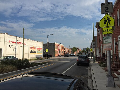 Hanover Street looking north, brick rowhouses and low rise commercial storefronts along an asphalt roadway with parking signs.