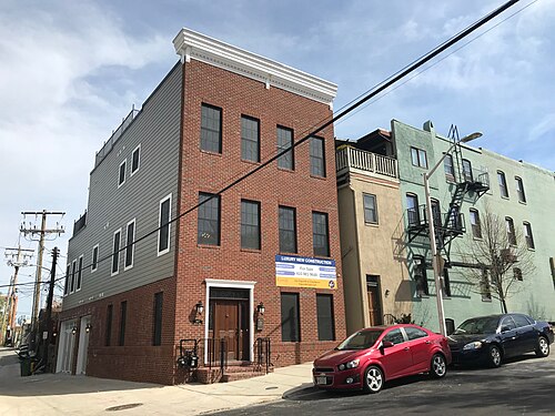 A red brick infill house on Webster Street standing beside older painted brick rowhouses, cars parked along the asphalt street.