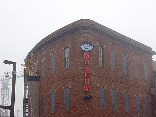 The corner of the American Visionary Art Museum at Key Highway, a rounded red brick building with a neon sign reading Museum Cafe.