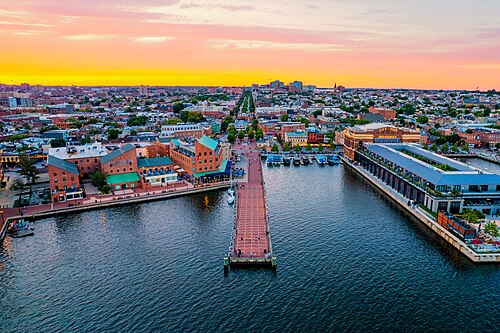 An aerial view at sunset over the harbor piers and brick rowhouse blocks, boats moored along a pier reaching into the water.
