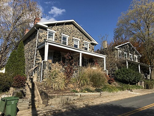 Two storey stone semi detached houses with covered porches and small front yards on a sloped street.