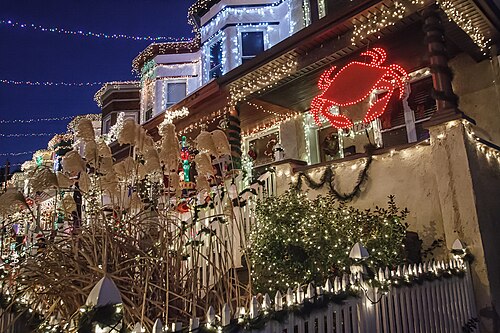Rowhouses on the 700 block of West 34th Street covered in dense Christmas light displays, a lit red crab sign among them.