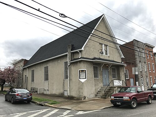A gabled stucco church on a street corner next to brick rowhouses.