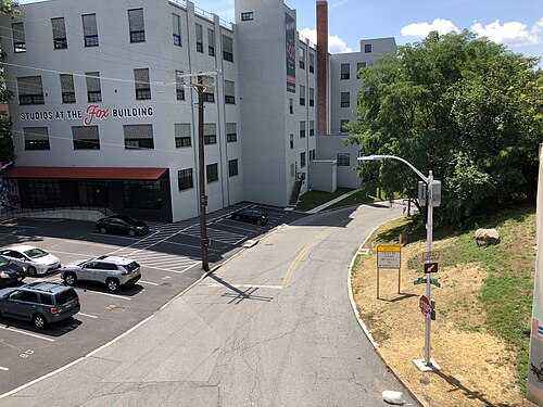 An elevated view of the Fox Building, a converted concrete mill building at Falls Road and Roland Avenue, its sign reading Studios at the Fox Building over a chimney and parking lot.