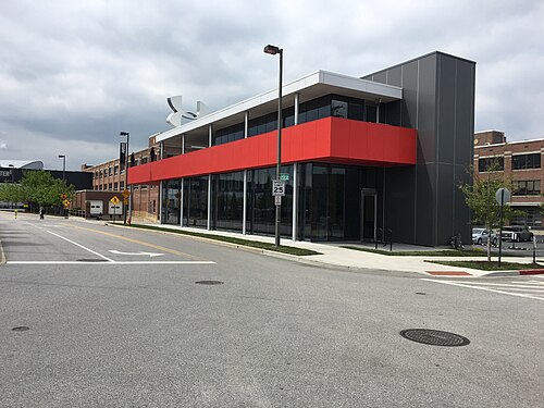 A low two storey building at Tide Point with dark panel cladding and a red banded upper floor, glass walled ground floor, an empty street in front.