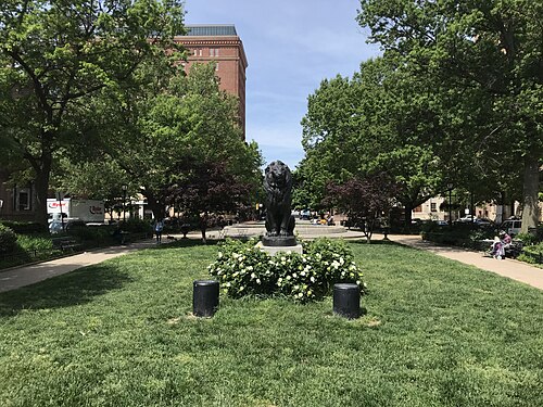 Barye's bronze Seated Lion on its stone plinth in the west park, townhouses lining the square behind it.