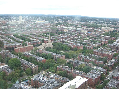 An aerial view over the Back Bay grid, rows of brick and brownstone rooftops running in straight lines with a church spire rising from the middle of the blocks.