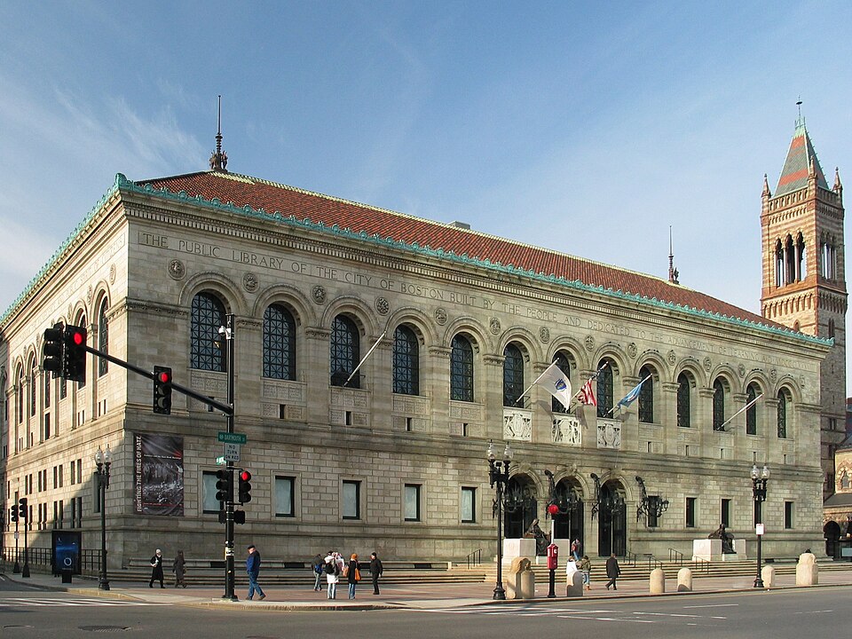 The Boston Public Library's Copley Square entrance in pale granite, three arched doorways under an inscription naming the building, flags over the steps.