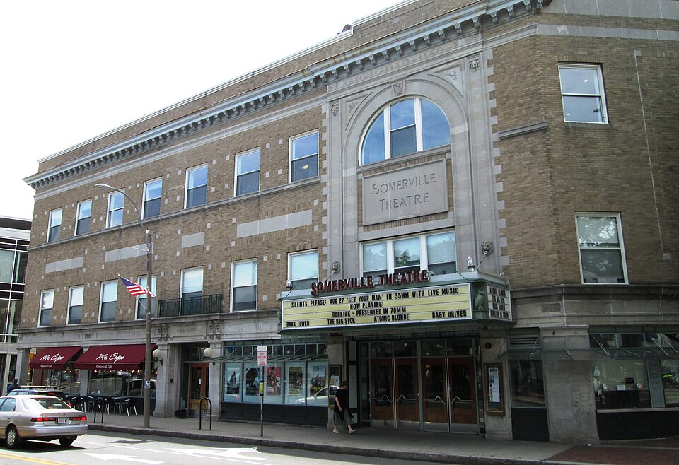 The Hobbs Building's full three storey brick facade, the theatre marquee and ground floor storefronts, a parked car and awnings along the sidewalk.