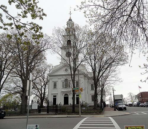 First Parish Church on Meeting House Hill, a white clapboard church with a tall tiered steeple behind a black iron fence, a Winter Street sign at the corner.
