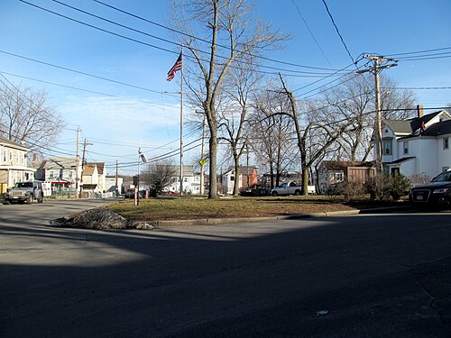 Doucette Square in Port Norfolk, a small triangular green with a flagpole, wood frame houses behind it and bare winter trees.