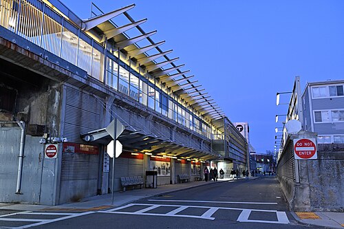 The rebuilt Fields Corner busway, a long steel and glass canopy over the platform with a lit red T sign at the far end.