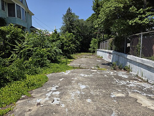 The fenced concrete roof of the Ashmont Branch tunnel, trees and the edge of a wood frame house visible past the chain link.