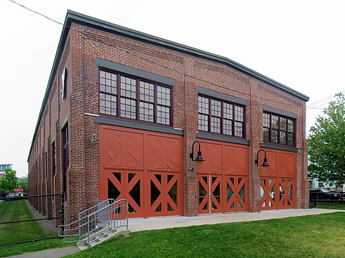 A long red brick engine house with arched multi pane windows and red barn style doors, the former railroad building now home to a YMCA, a lawn out front.