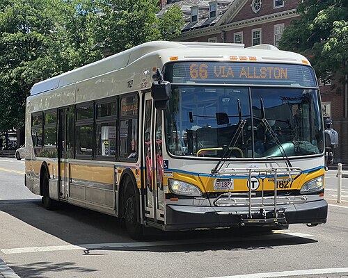 An MBTA bus signed 66 VIA ALLSTON stopped at a street corner, trees and a red brick Harvard building behind it.