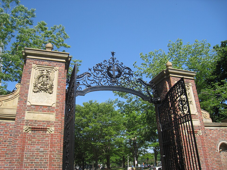Johnston Gate's wrought iron gates between red brick piers, a carved eagle and wreath crest over the arch, trees inside the Yard behind it.