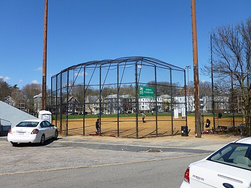 A chain link backstop cage at Murphy Playground, triple decker rooftops lined up behind the outfield fence.
