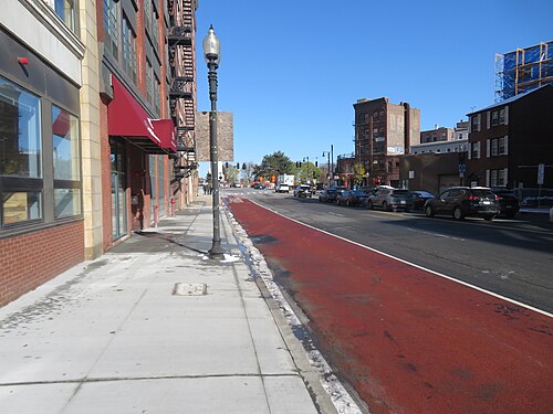 North Washington Street on the neighborhood's western edge, a red painted bus lane along the curb, a red brick apartment building with a fire escape and a red awning at the corner.