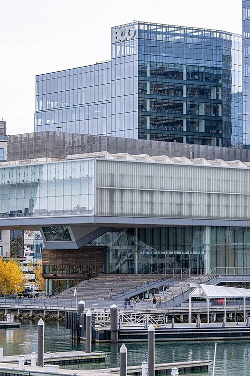 A glass tower marked BCG behind the Institute of Contemporary Art, whose glass box cantilevers out over the water with a wide outdoor stair running down to the harbor.