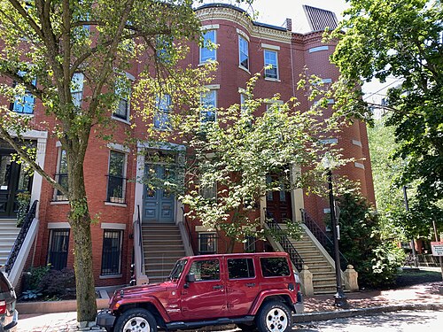 A single bowfront rowhouse on Yarmouth Street, paired stone stoops with wrought iron rails leading to arched doorways, a red SUV parked at the curb.