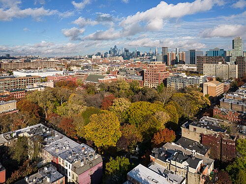 An elevated view over brownstone rooftops around the park, with the Manhattan skyline visible on the horizon.