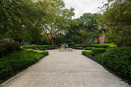 A paved path lined with hedges leading to the park's central fountain.
