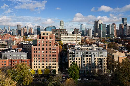 An elevated view of brick and newer apartment buildings along a street bordering the park, park trees in the foreground.