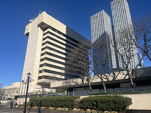 The transportation center's concrete tower with a Duane Reade and Starbucks at its base, glass residential towers rising behind it, hedges lining the plaza.