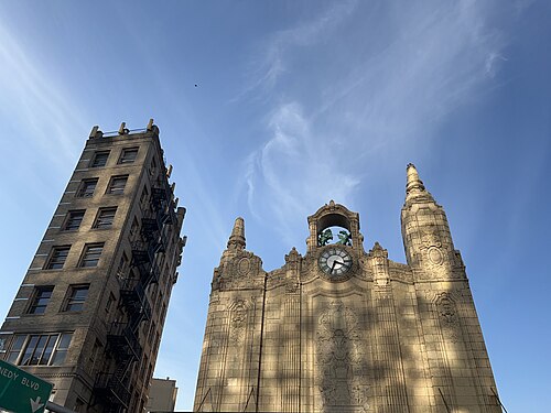 A low angle view of the theatre's cream terracotta facade, the round clock flanked by carved pinnacles against the sky.