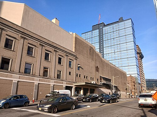 The Stanley Theater's rear elevation in tan brick, arched window traces on its upper floor, beside a glass apartment tower under construction with a crane overhead.