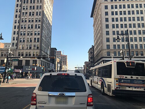 Broad Street's canyon of stone office towers, a city bus ahead and a Broad St sign at the corner.