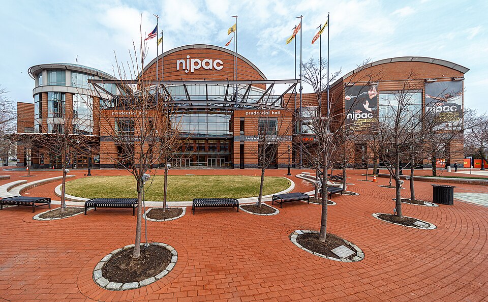 The New Jersey Performing Arts Center's brick entrance, Prudential Hall spelled out over the doors and a plaza of benches in front.