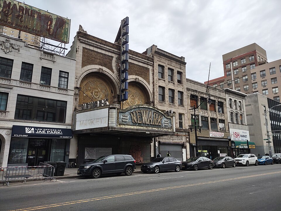 Market Street storefronts beside the shuttered Paramount Theatre, its marquee still spelling out NEWARK over roll down gates.