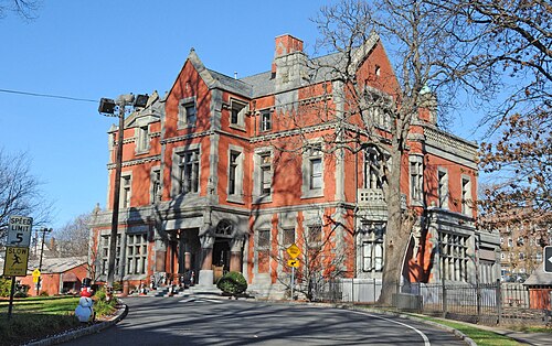 The William Clark House, a three storey red brick mansion with stone trim, steep gables and a chimney, behind a curved driveway and an iron fence.