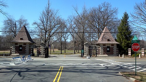 The Ballantine Gateway, two steep roofed stone gatehouses framing the road into Branch Brook Park, with the Ballantine Parkway and Lake Street signs at the corner.