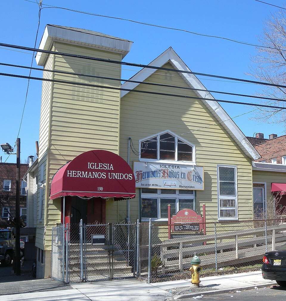 A yellow sided wood frame house at 190 Highland Avenue, converted into a storefront church with a red entrance awning, behind a chain link fence.