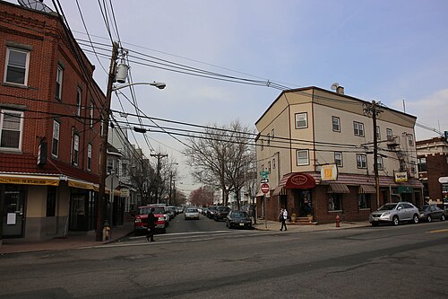 A cream sided corner building with striped awnings over a boutique storefront, looking down a side street of parked cars.
