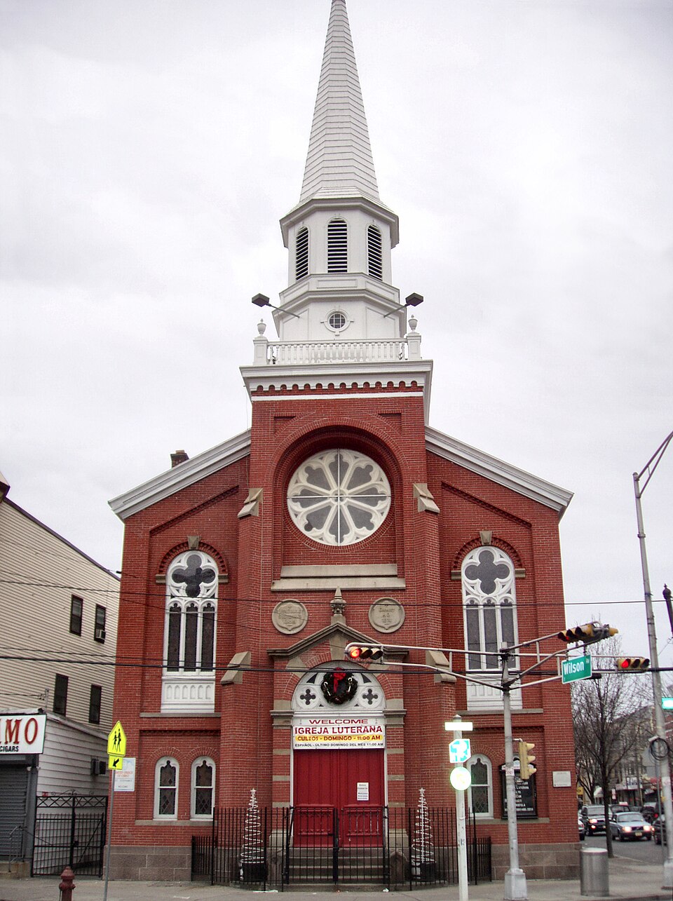 The red brick Romanesque front of St. Stephan's Church, a rose window under the gable and a white steeple over an open lantern, the Wilson Avenue street sign at the corner.
