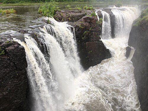 Looking upstream from the footbridge at the several channels of the falls pouring over the basalt ledge, a wide slow river above it.