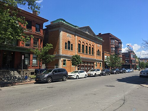 A street corner of brick commercial and theatre buildings on Allen Street, parked cars and trees along the sidewalk.